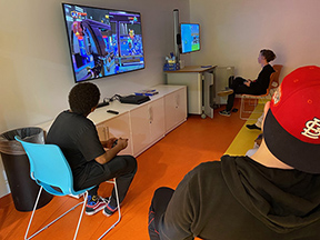 Accompanied by a residential team member, two Five Acres children take a break from remote learning and play video games in the new teen room in the auditorium while practicing social distancing.