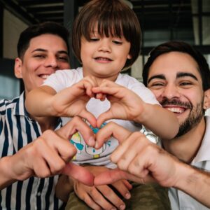 A gay couple with a young toddler son making heart shapes with their hands